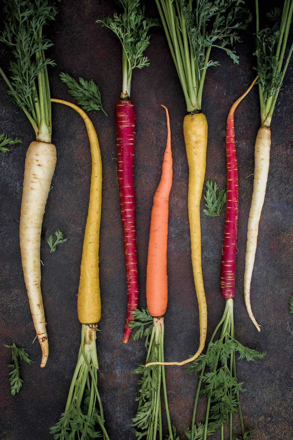 Five rainbow carrots on a rustic background.