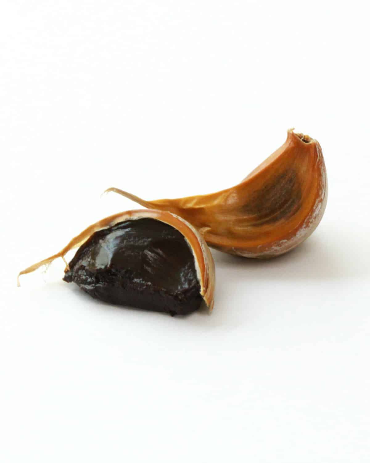 Two cloves of black garlic with one clove peeled.