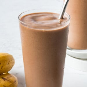 Nutella banana smoothie with a metal straw, with banana on the left and Nutella banana milkshake on the right.