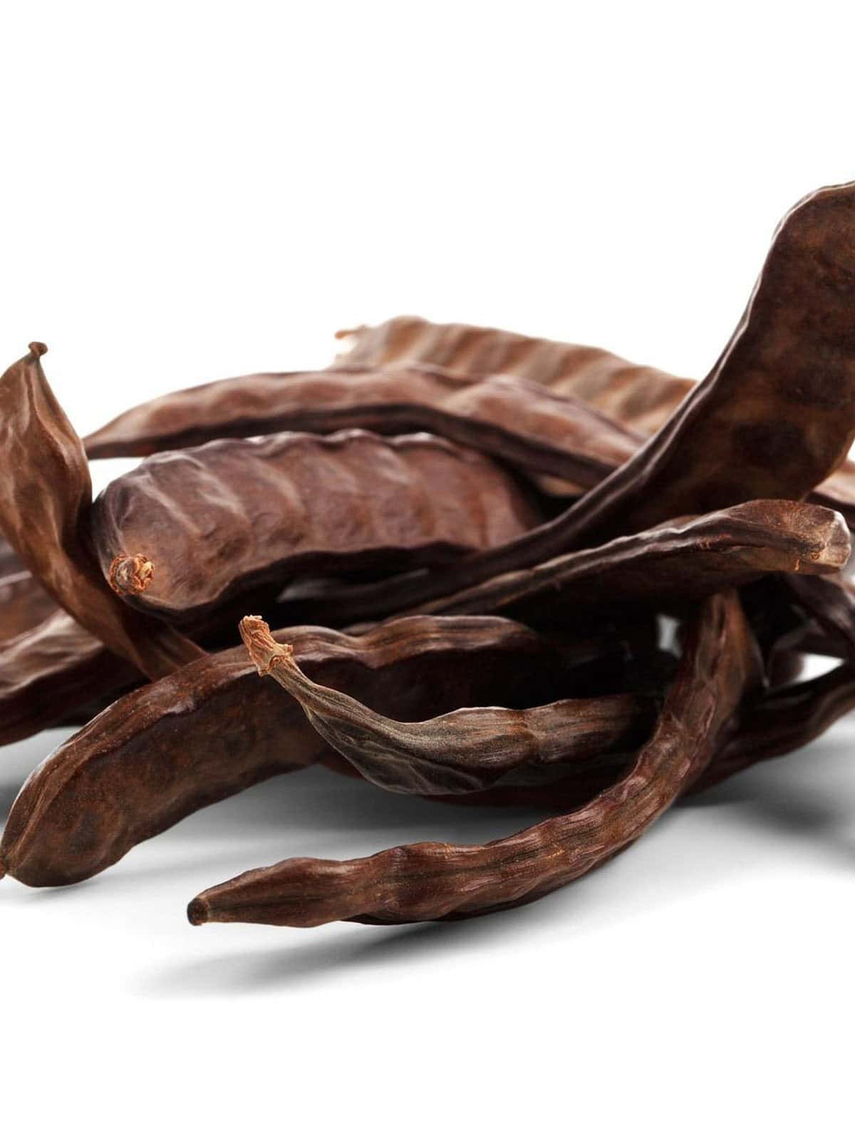 Dried brown carob pods on a white background.