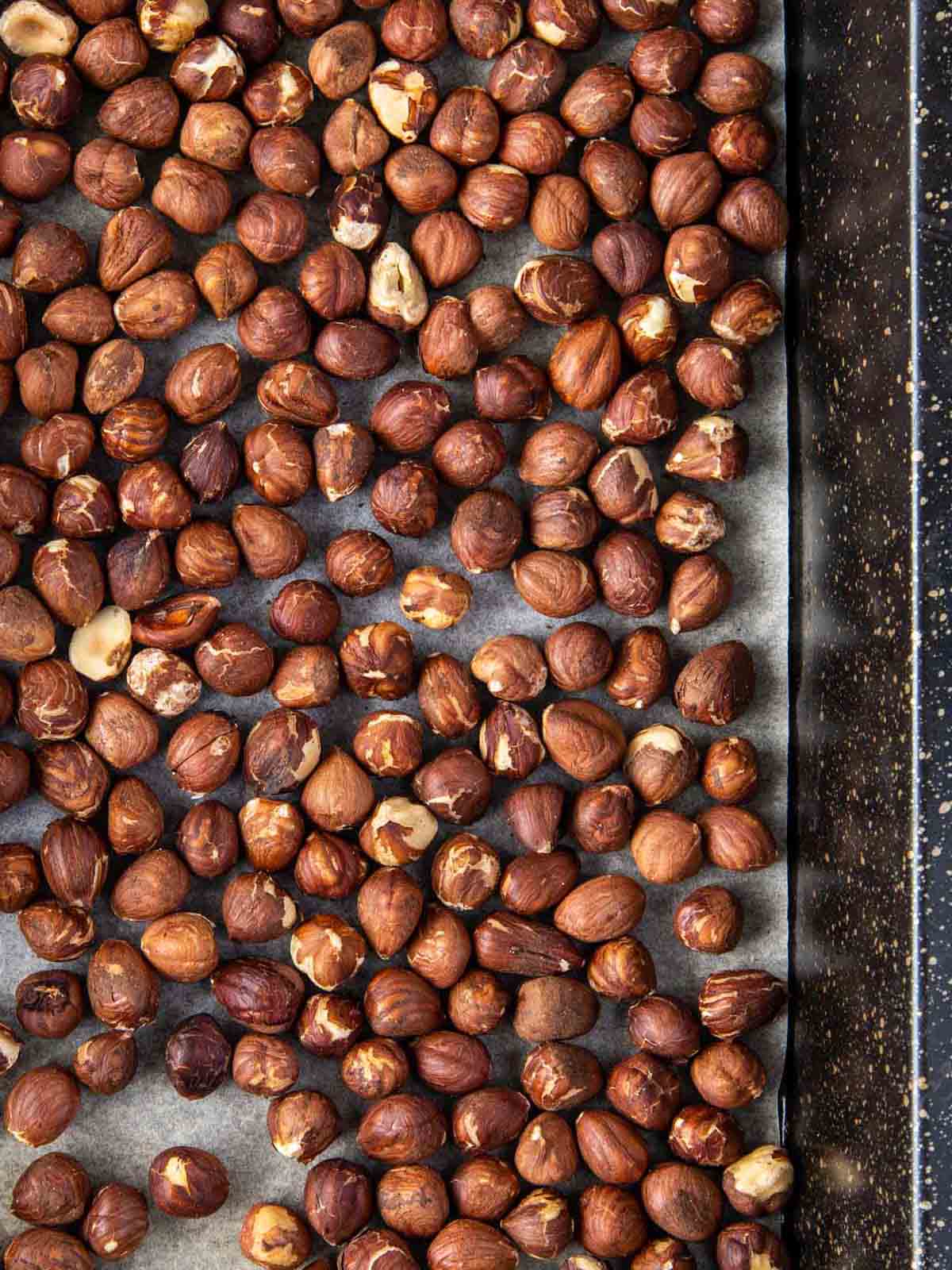 Roasted brown hazelnuts on a roasting tray.