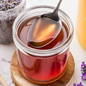 Close-up of honey lavender simple syrup with a spoon in a glass jar.