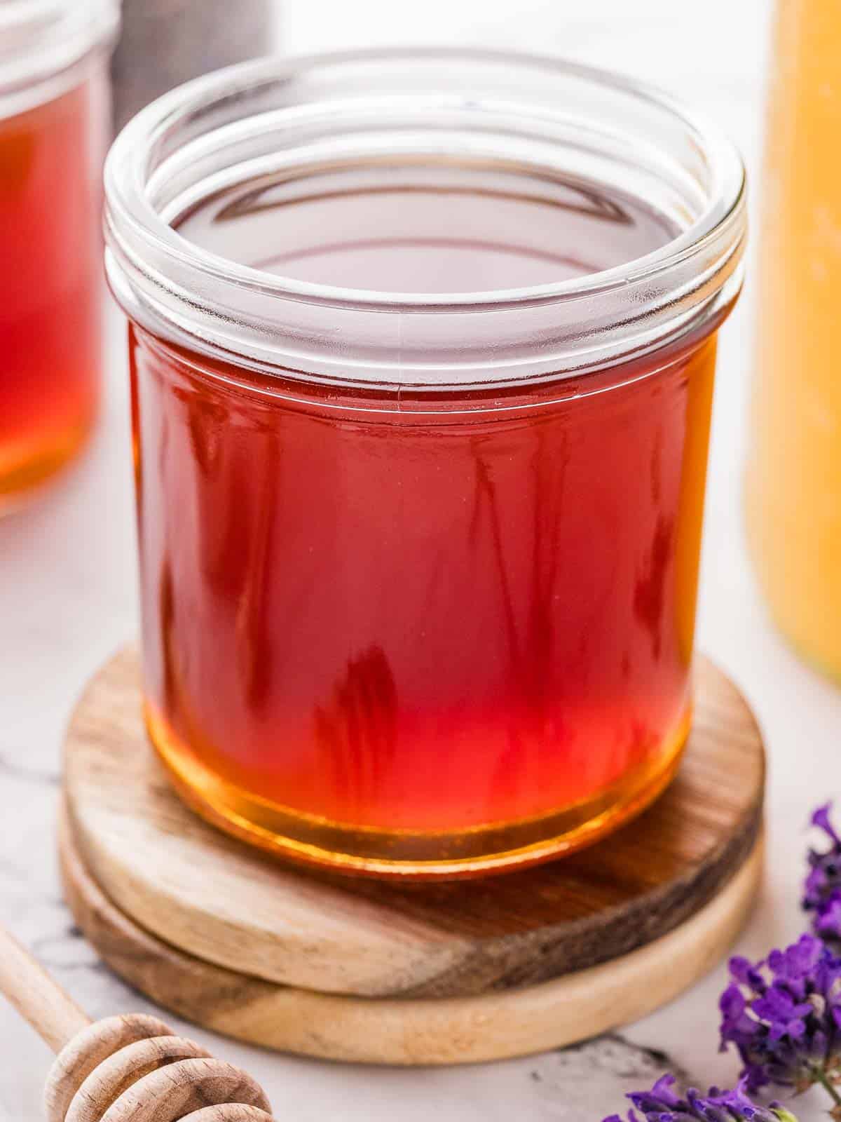 A glass of honey lavender simple syrup on top of two wooden coasters.
