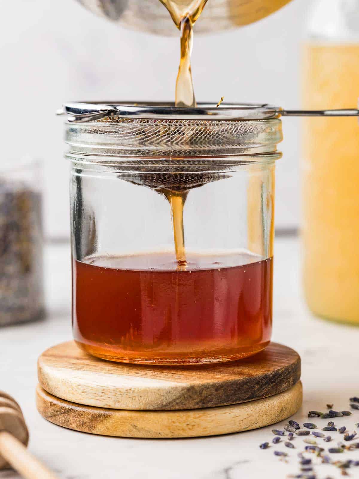 Straining lavender honey through a fine mesh sieve into a glass jar.
