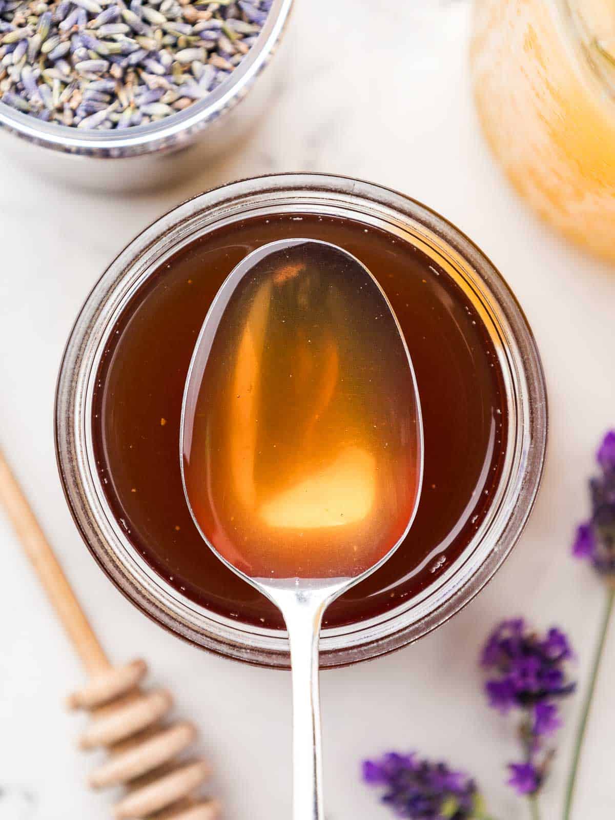 Close-up of a spoonful of lavender honey simple syrup taken from above, with more lavender around it.