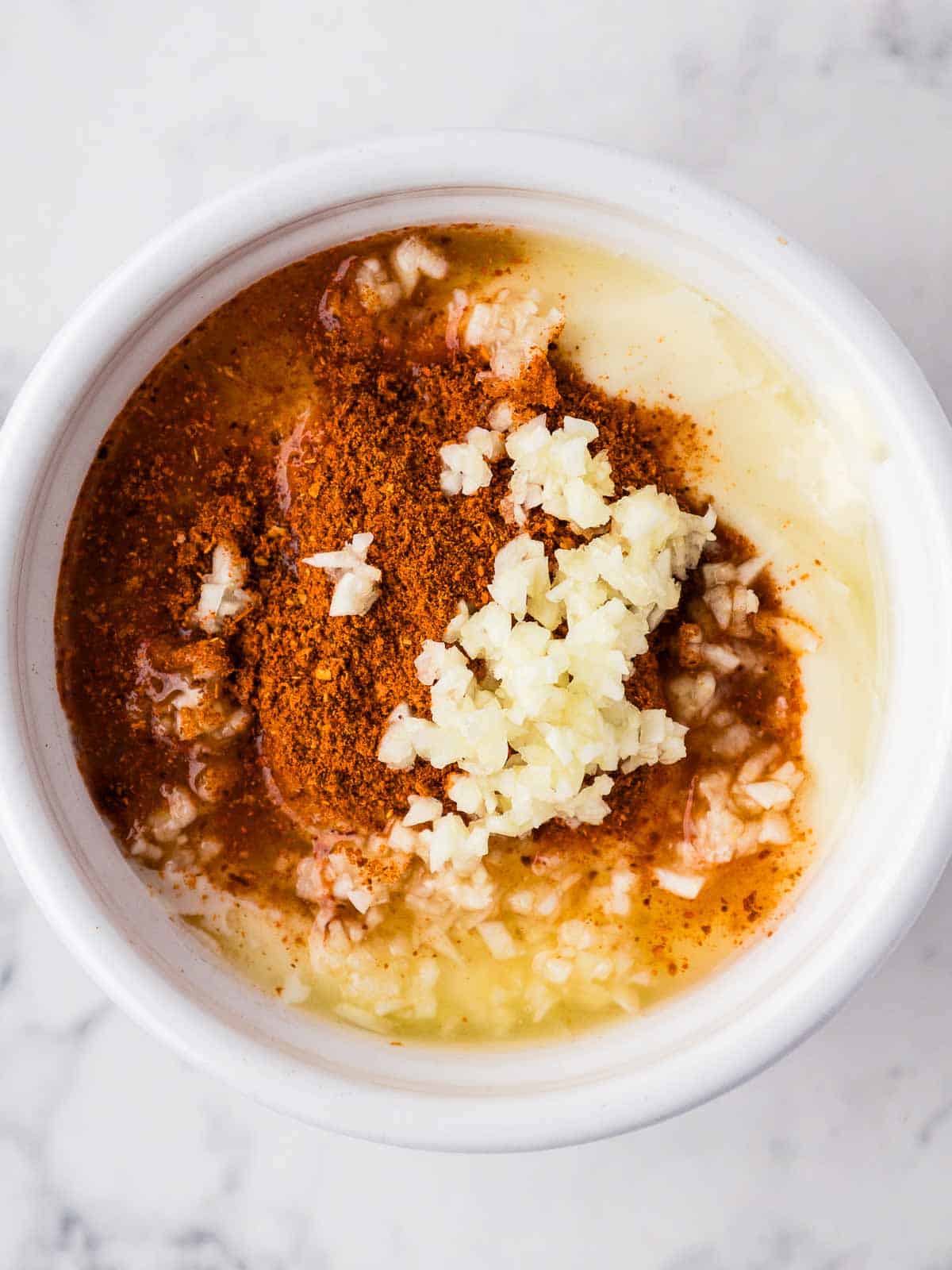 Mayonnaise, lemon juice, cayenne pepper, and minced garlic in a small white ramekin.