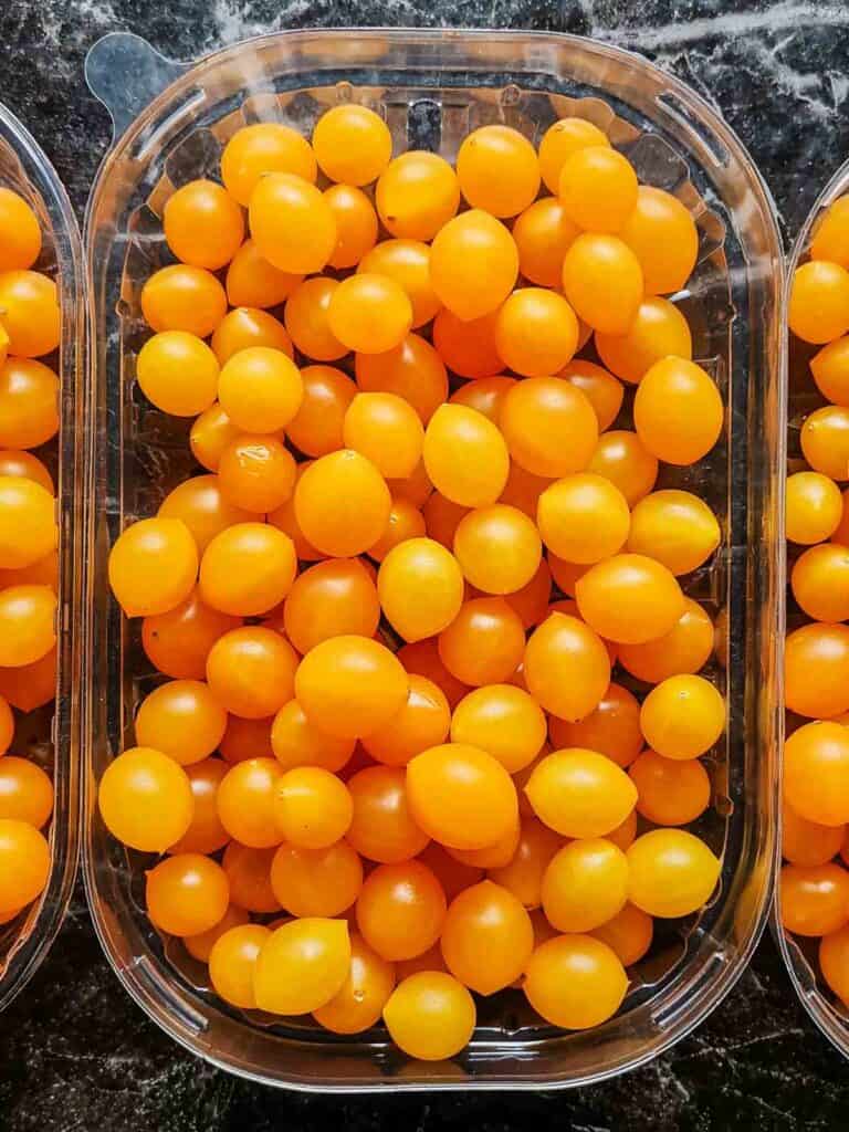 A bunch of orange currant tomatoes on a plastic lid, on a black marbled background.