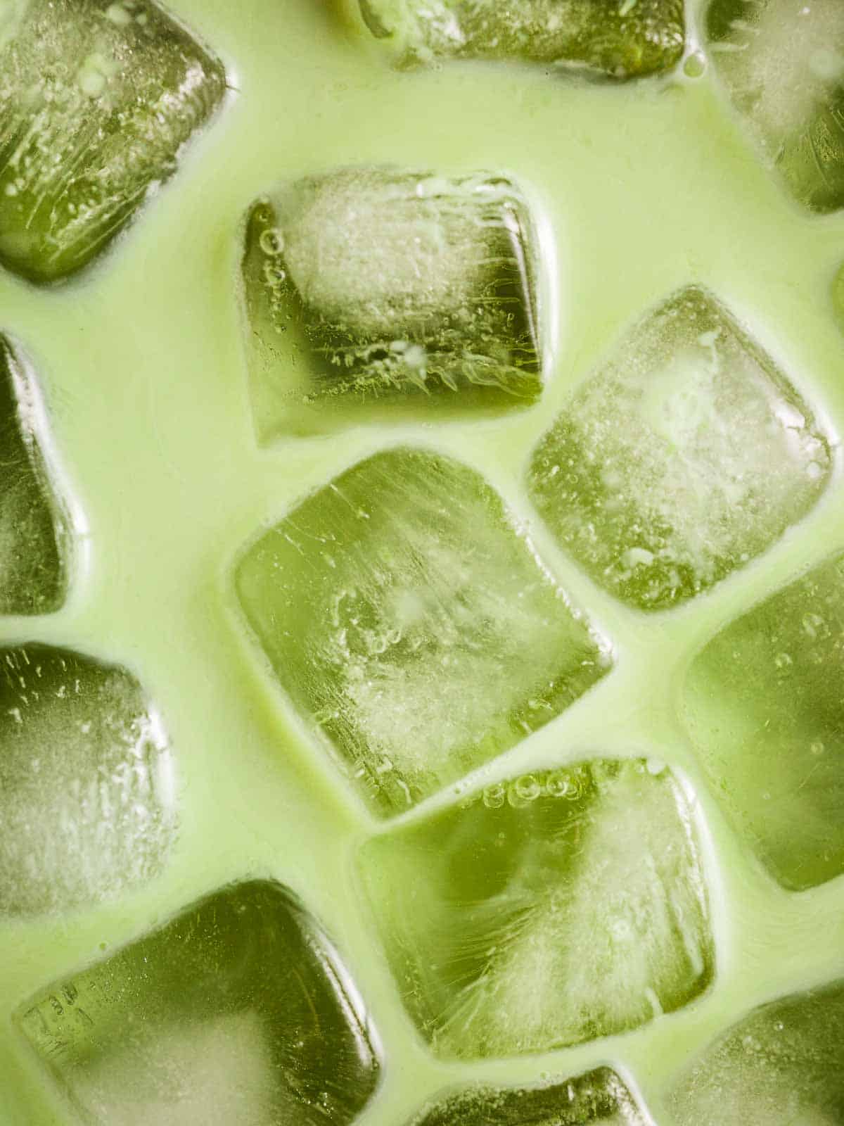 Close-up of ice cubes in matcha latte with vanilla extract.