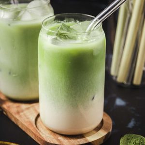 Iced vanilla matcha latte drinks served on a wooden plank.