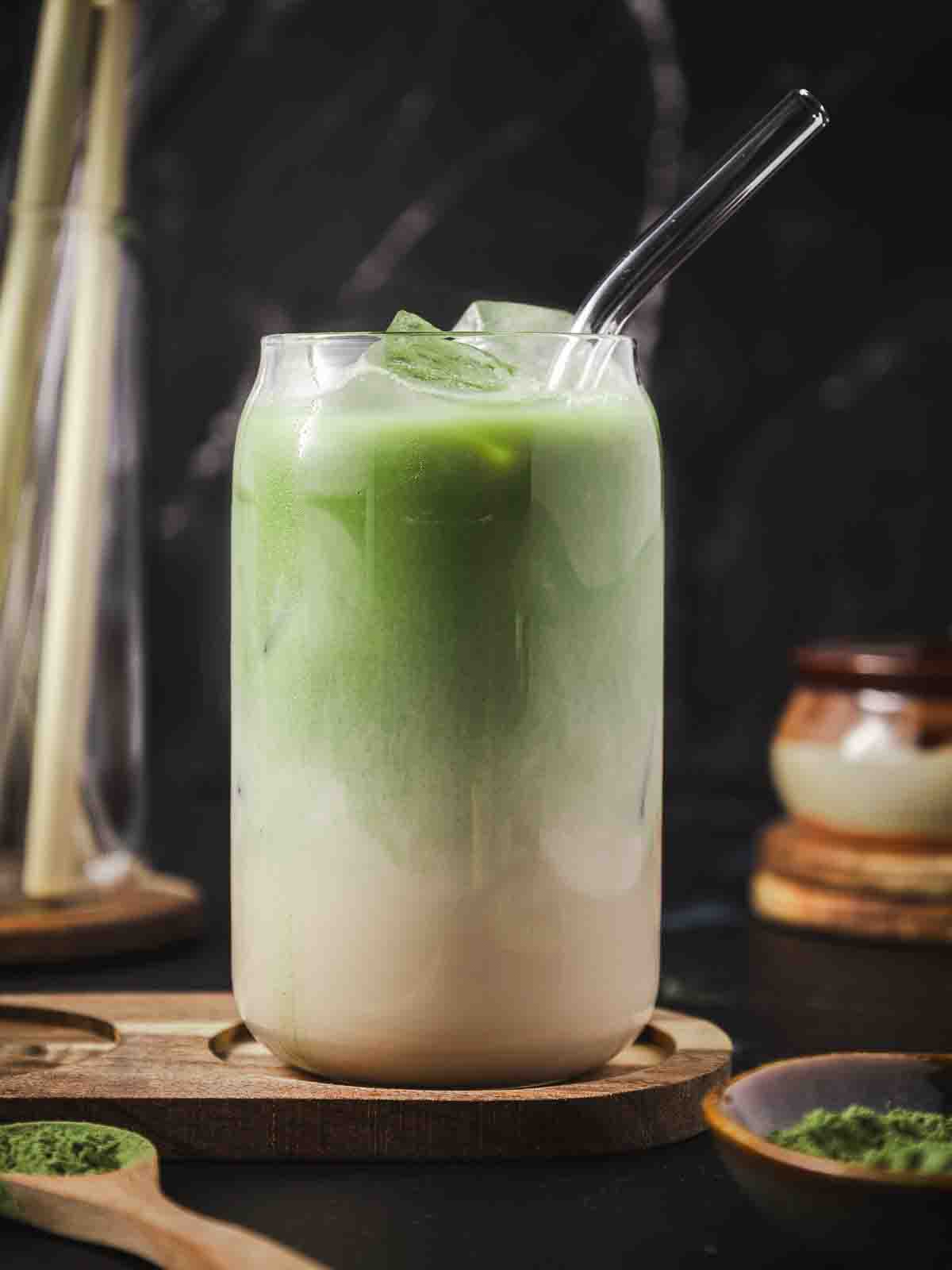 A glass of iced matcha vanilla latte with a glass straw.