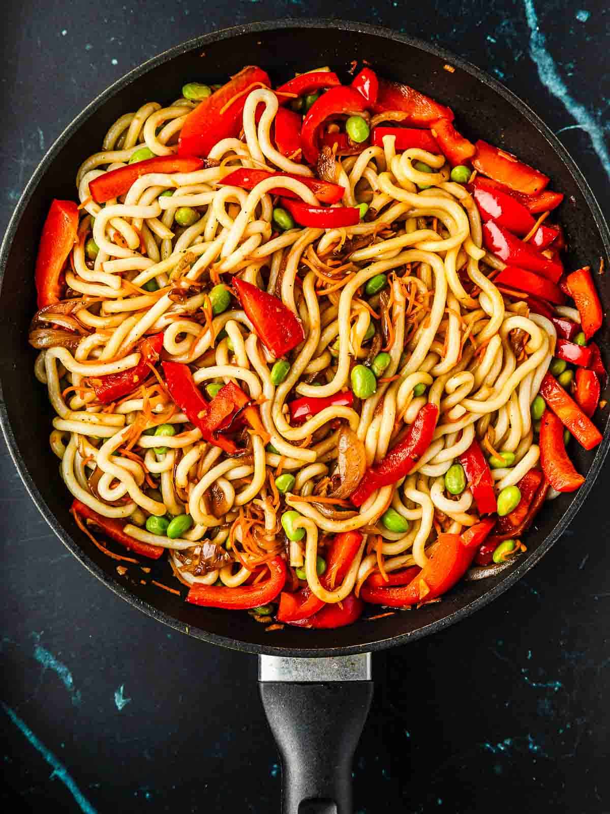 A pan of vegetarian teriyaki noodles with red bell pepper and edamame.
