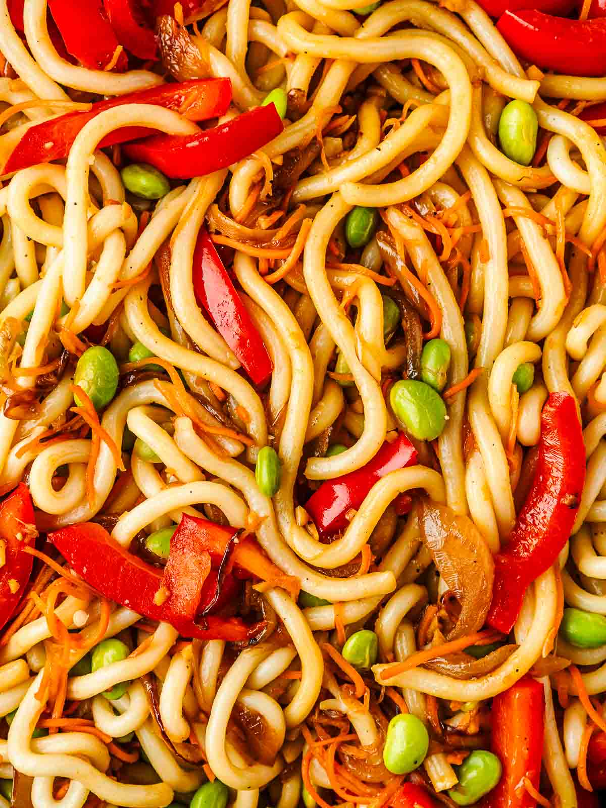 Close-up of vegetable udon noodles with carrots, red bell pepper, and edamame beans.