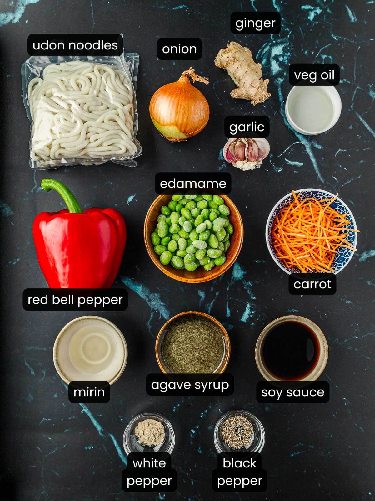 Ingredients for vegan teriyaki noodles with labels on a black marbled background.