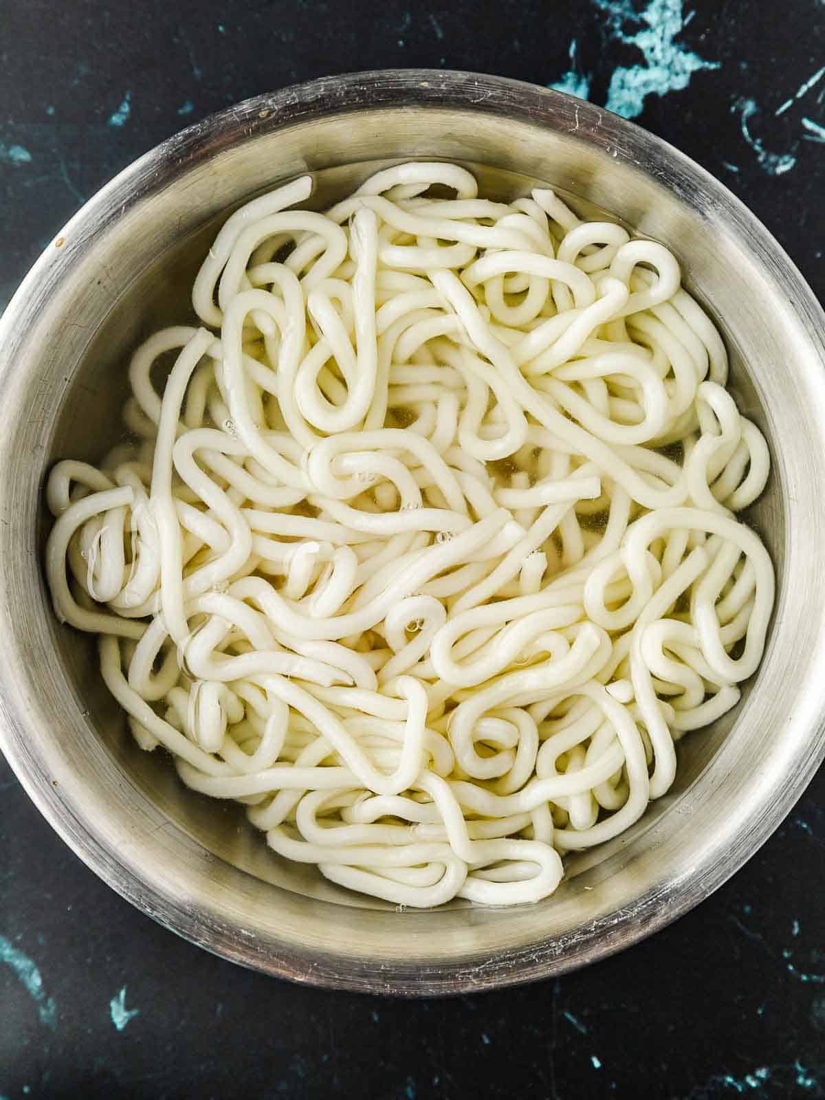 Loosened up udon noodles in a big bowl of hot water.