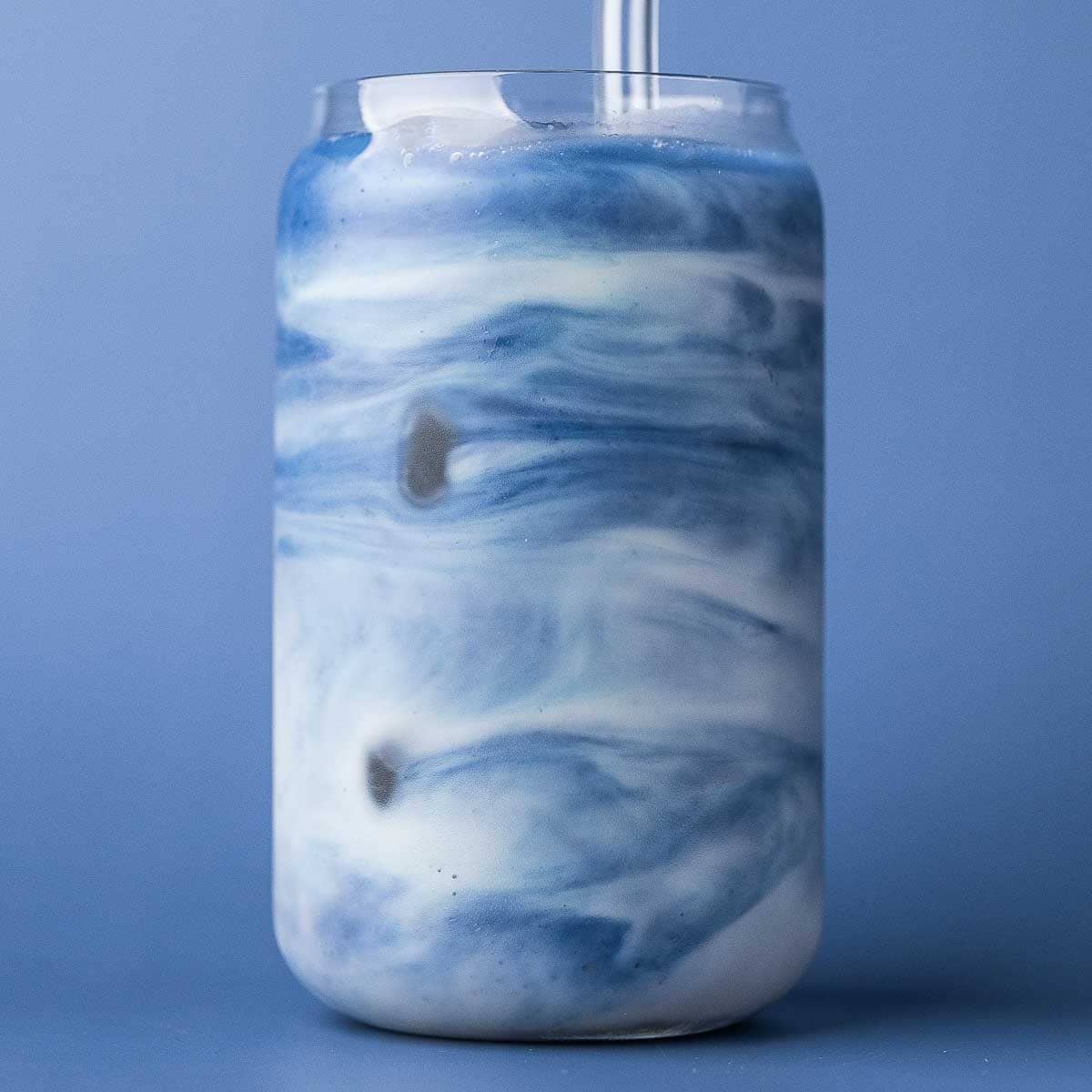 Blue matcha latte, made with butterfly pea flower powder, being stirred to create a marbled look.